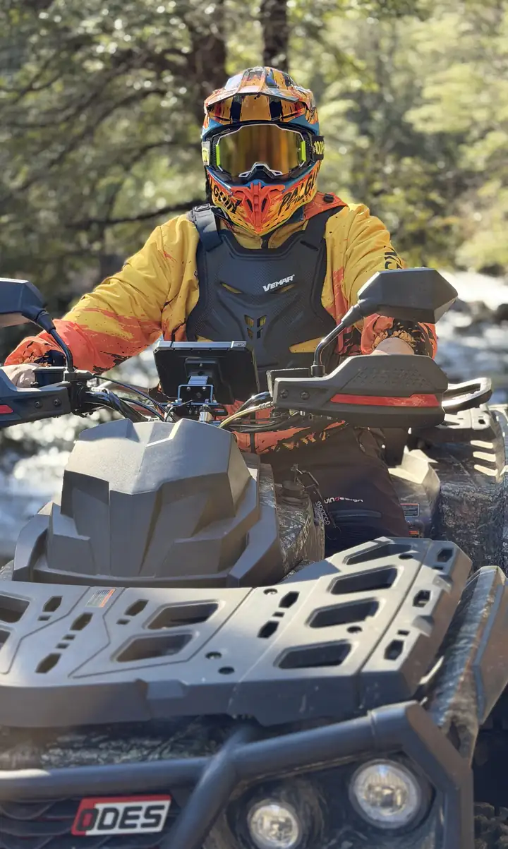 Piloto en cuatrimoto con casco integral, antiparras y protector de pecho, junto al río en el bosque nativo del sector de Palguín