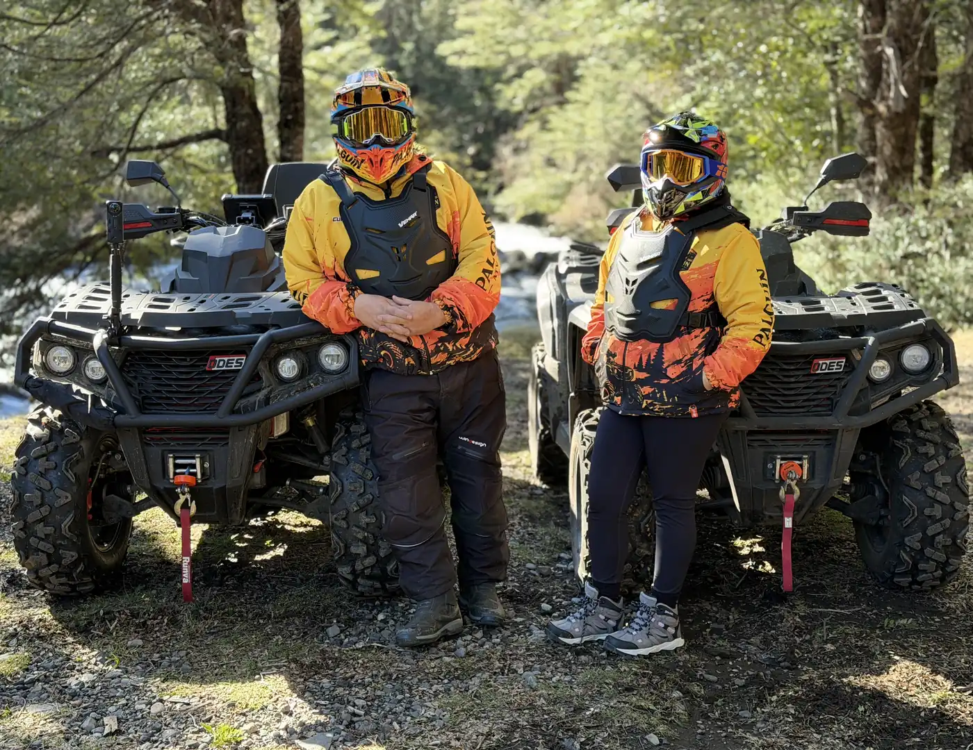 Dos integrantes de la familia de Palguín ATV Tour apoyados en sus cuatrimotos junto al río, con el bosque nativo de fondo